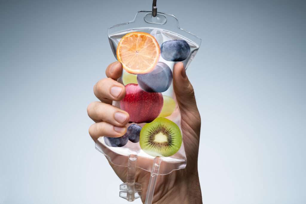 Hand holding a glass of fruit-infused water representing nutrition and vitamin support.