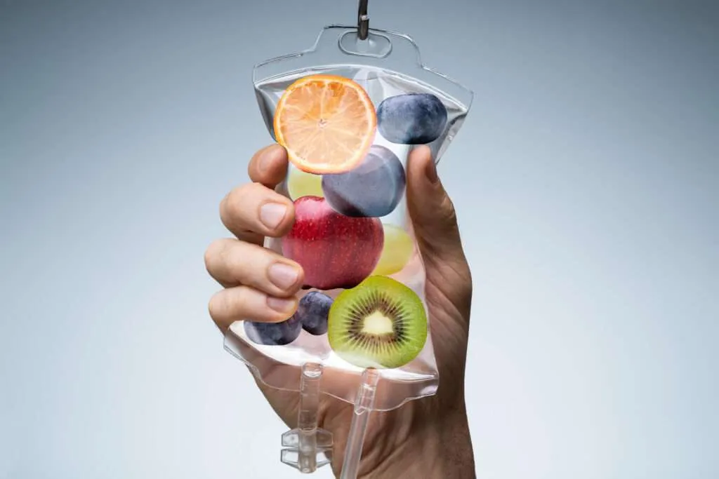 Hand holding a glass of fruit-infused water representing nutrition and vitamin support.
